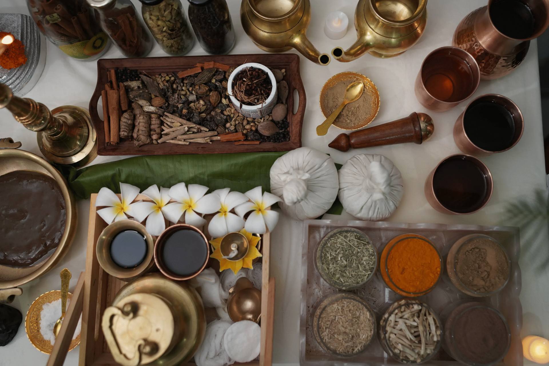 Ayurvedic herbal potli bundles, white flowers and therapy oils laid out for treatment