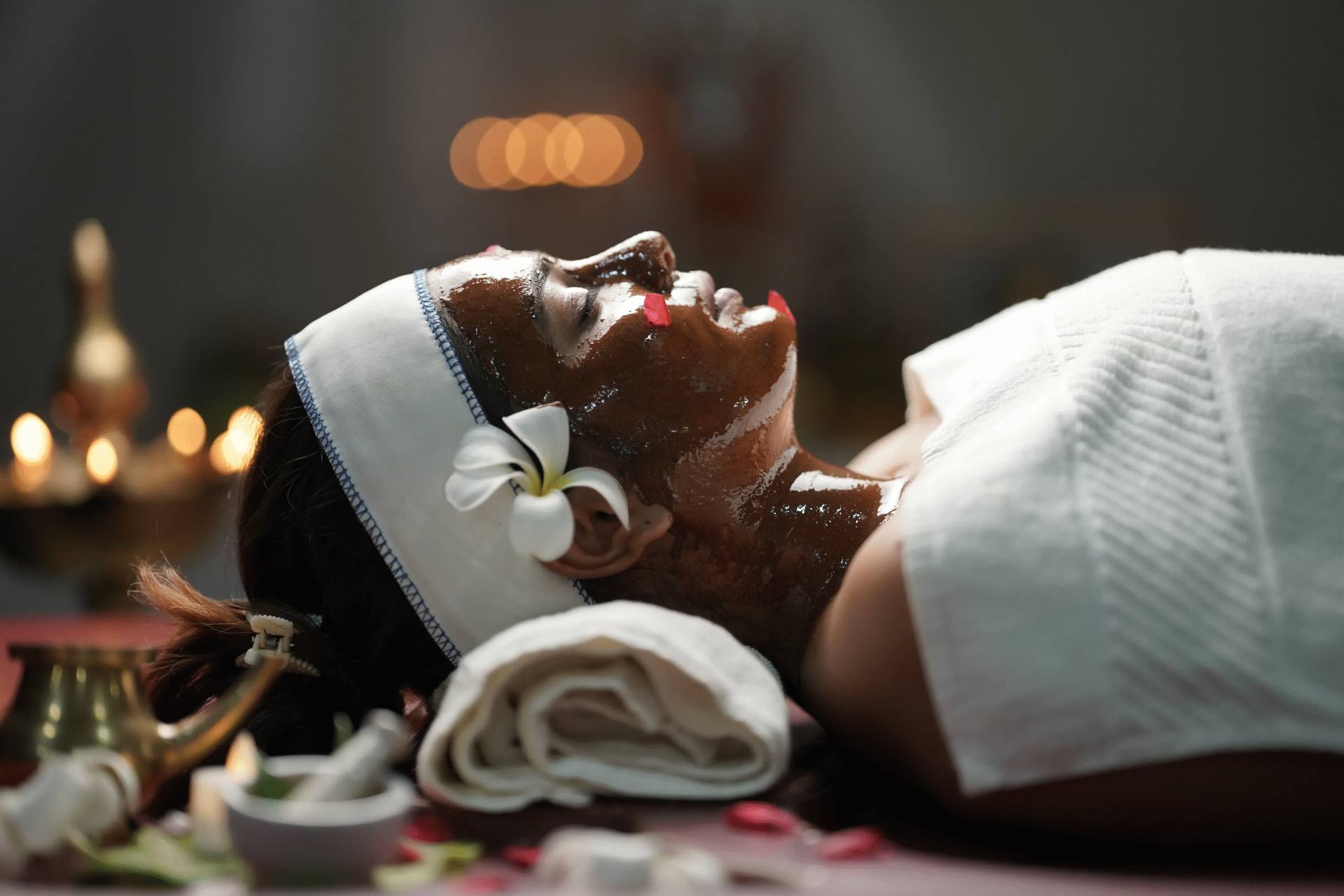 Patient relaxing with a herbal face pack and head wrap during an Ayurvedic therapy session